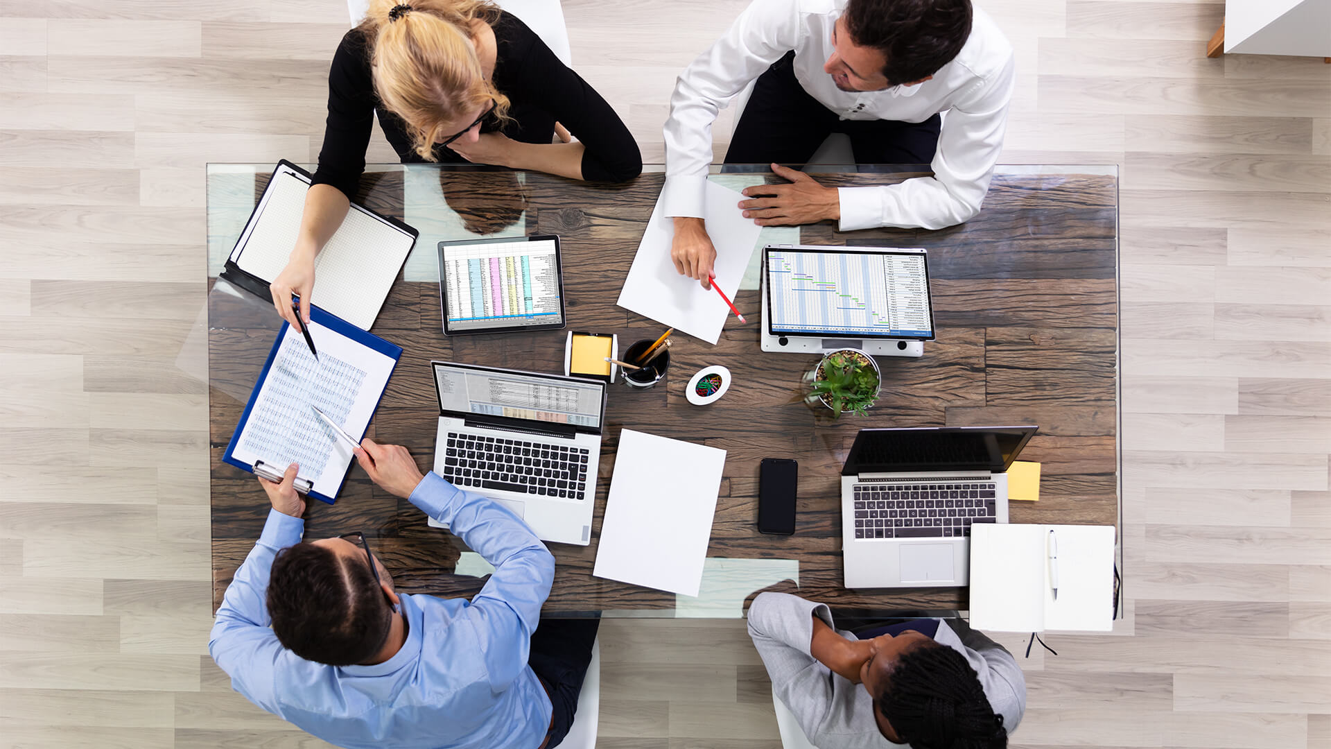 Four people working together at a table. Angle is from above looking down. They are working on laptops and looking at reports