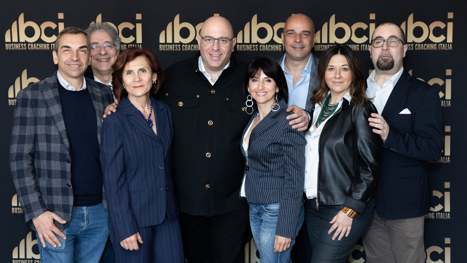 business people standing in front of wall with logos smiling at camera