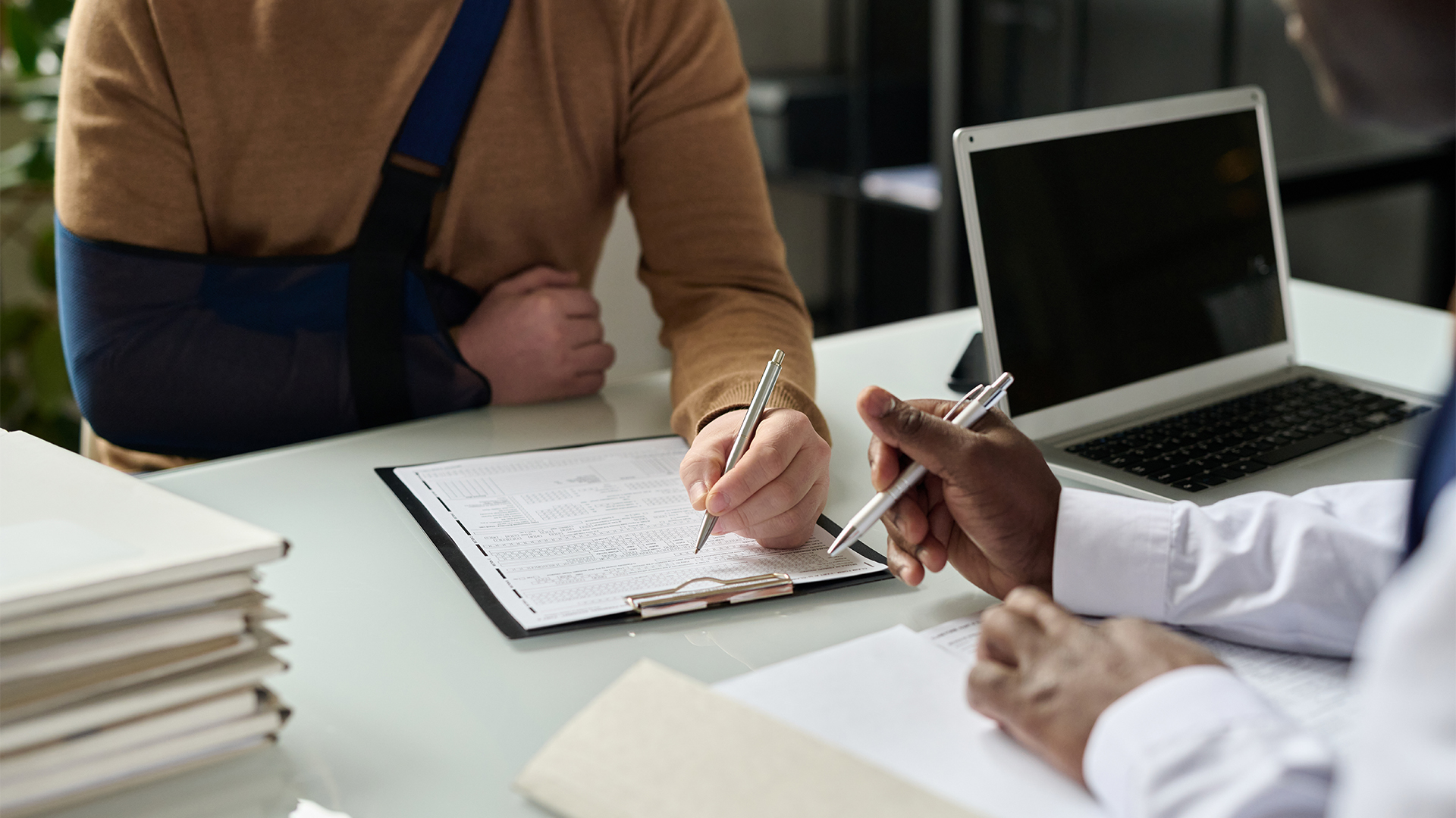 Close up of man filling in medical insurance form, injured hand in sling in background, copy space